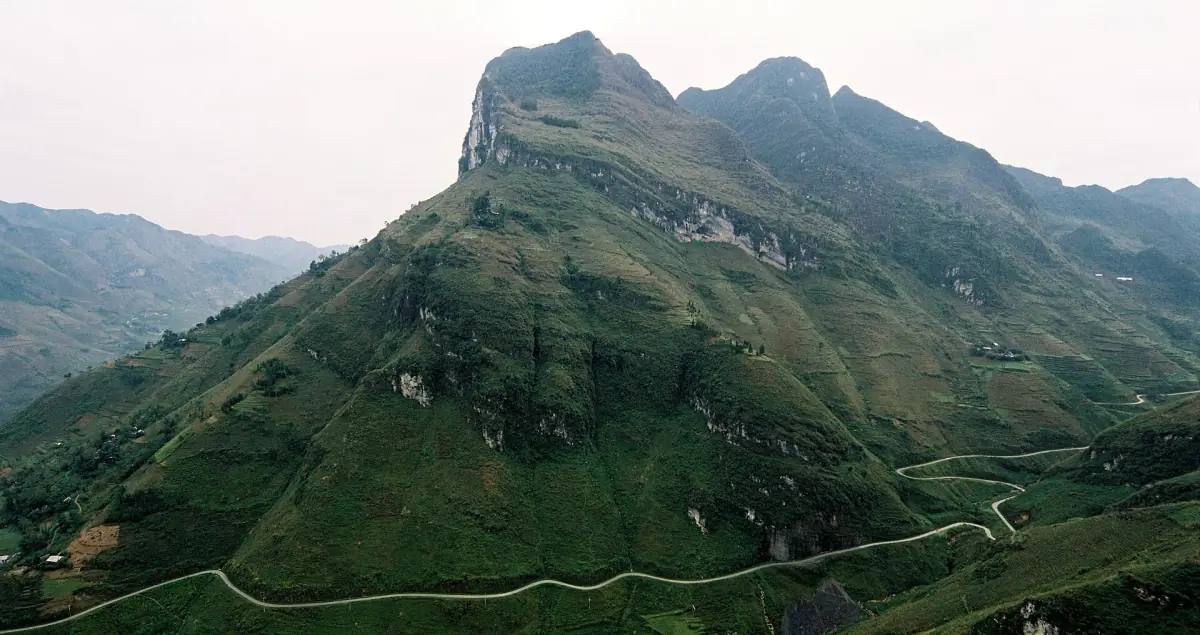 Kurvige Straße unter einem felsigen grünen Gipfel am Ma Pi Leng Pass in Ha Giang